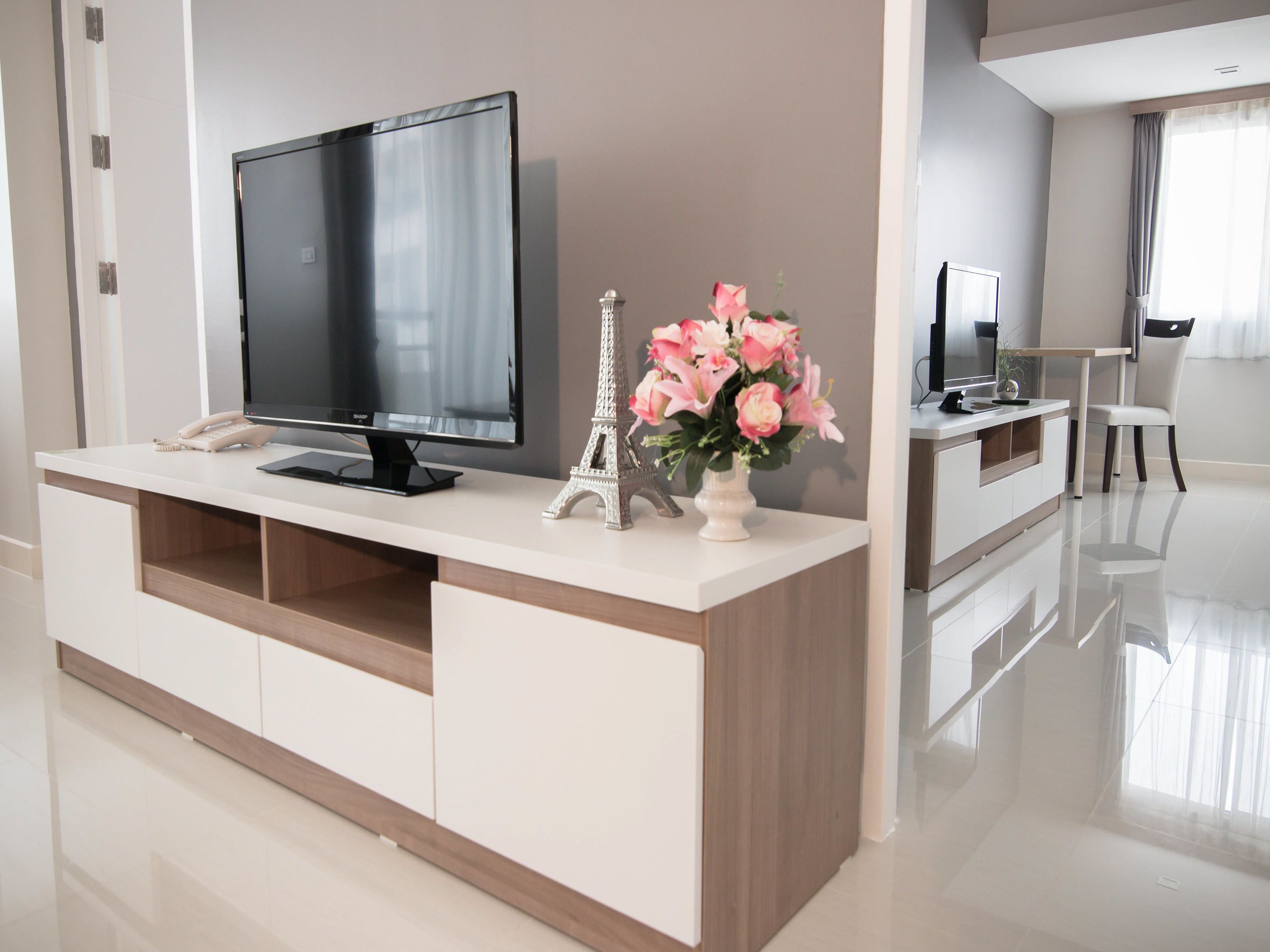 A modern living room with a flat-screen TV, a decorative Eiffel Tower, and a vase of pink flowers on a white console table.