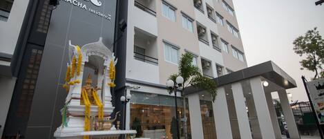 Exterior de un hotel con una estatua de una deidad, un cartel que dice 'RCHA residence' y un edificio moderno con balcones.