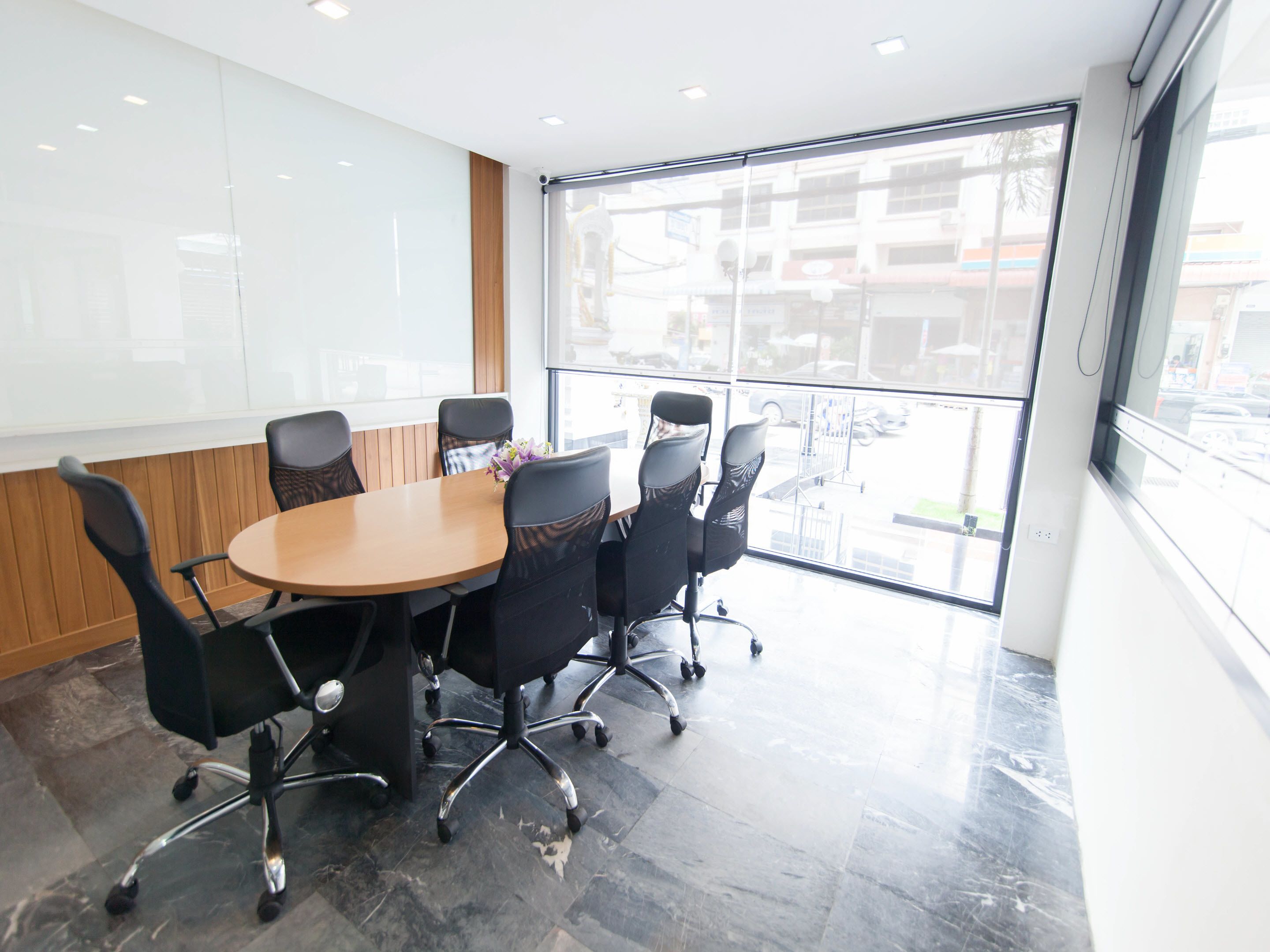A conference room with a round table and six chairs, large windows with a view of buildings, and a whiteboard on the wall.