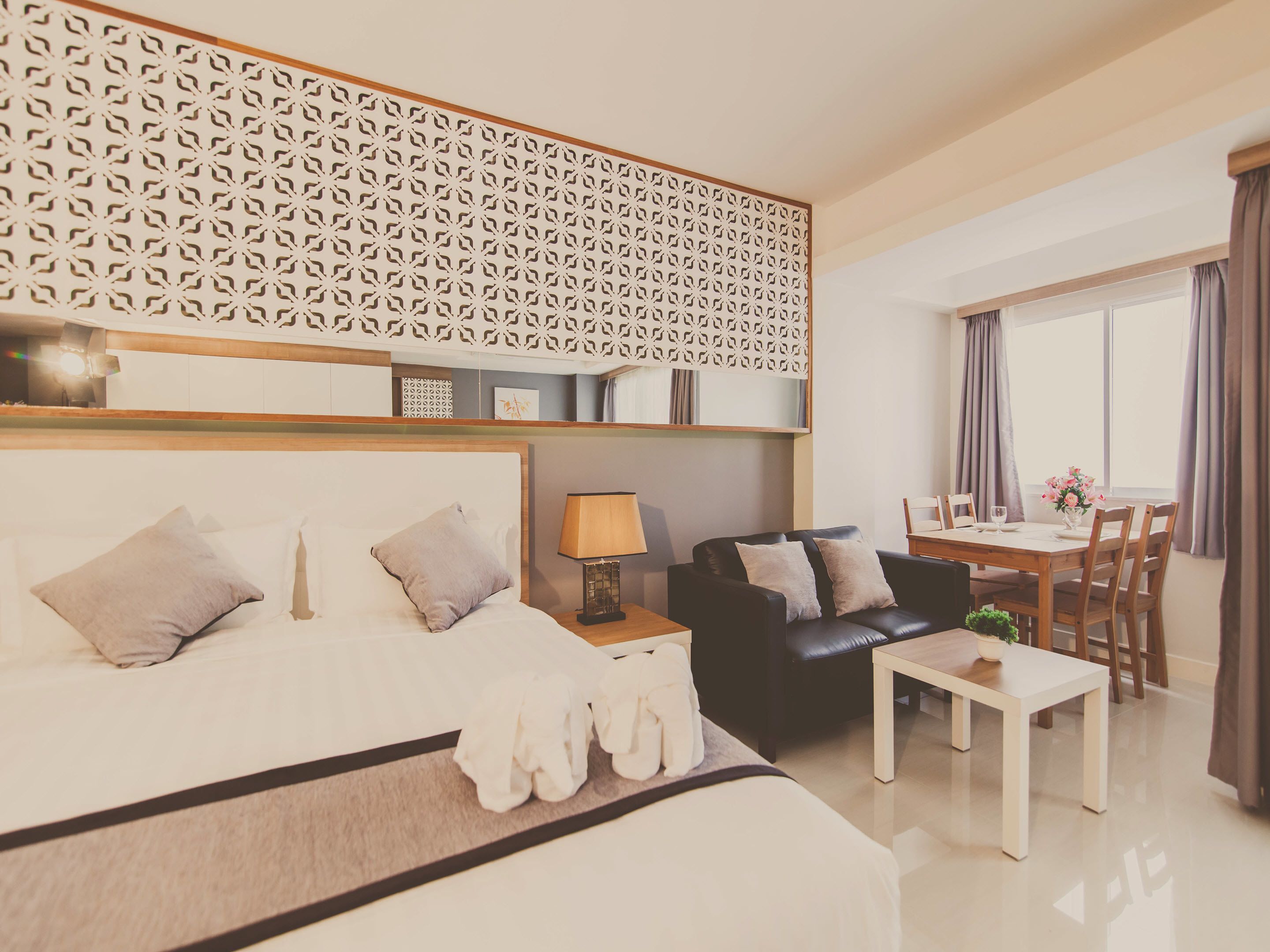 Una habitación de hotel moderna con una cama grande, un sofá de cuero negro, una mesa de comedor con sillas y un panel decorativo en la pared.