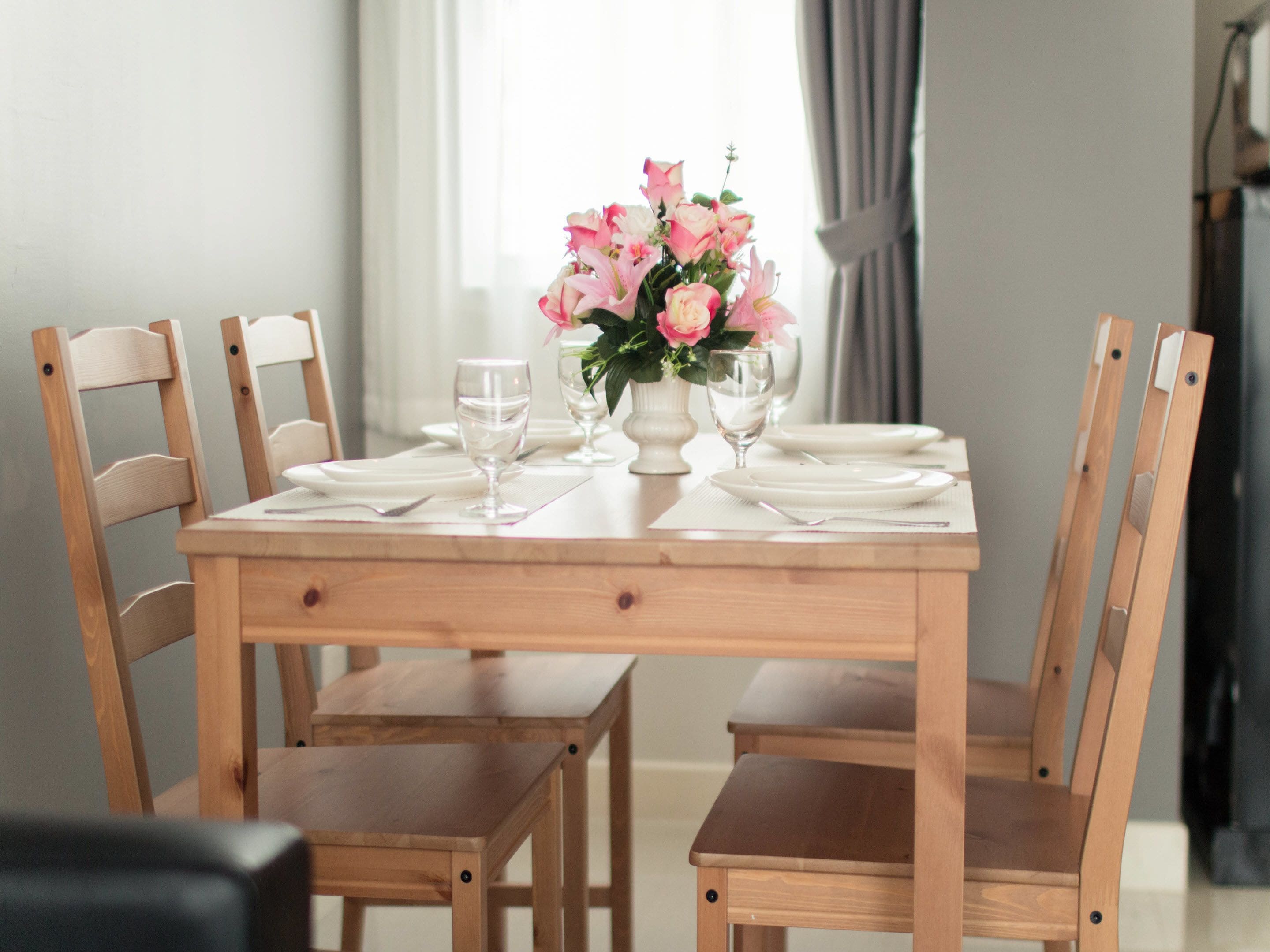 A dining table set with white plates, glasses, and a vase of pink flowers.