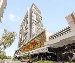 A modern building with a prominent vertical design, a retail and dining area, and a parking lot with cars. - The Milton Brisbane (Milton)