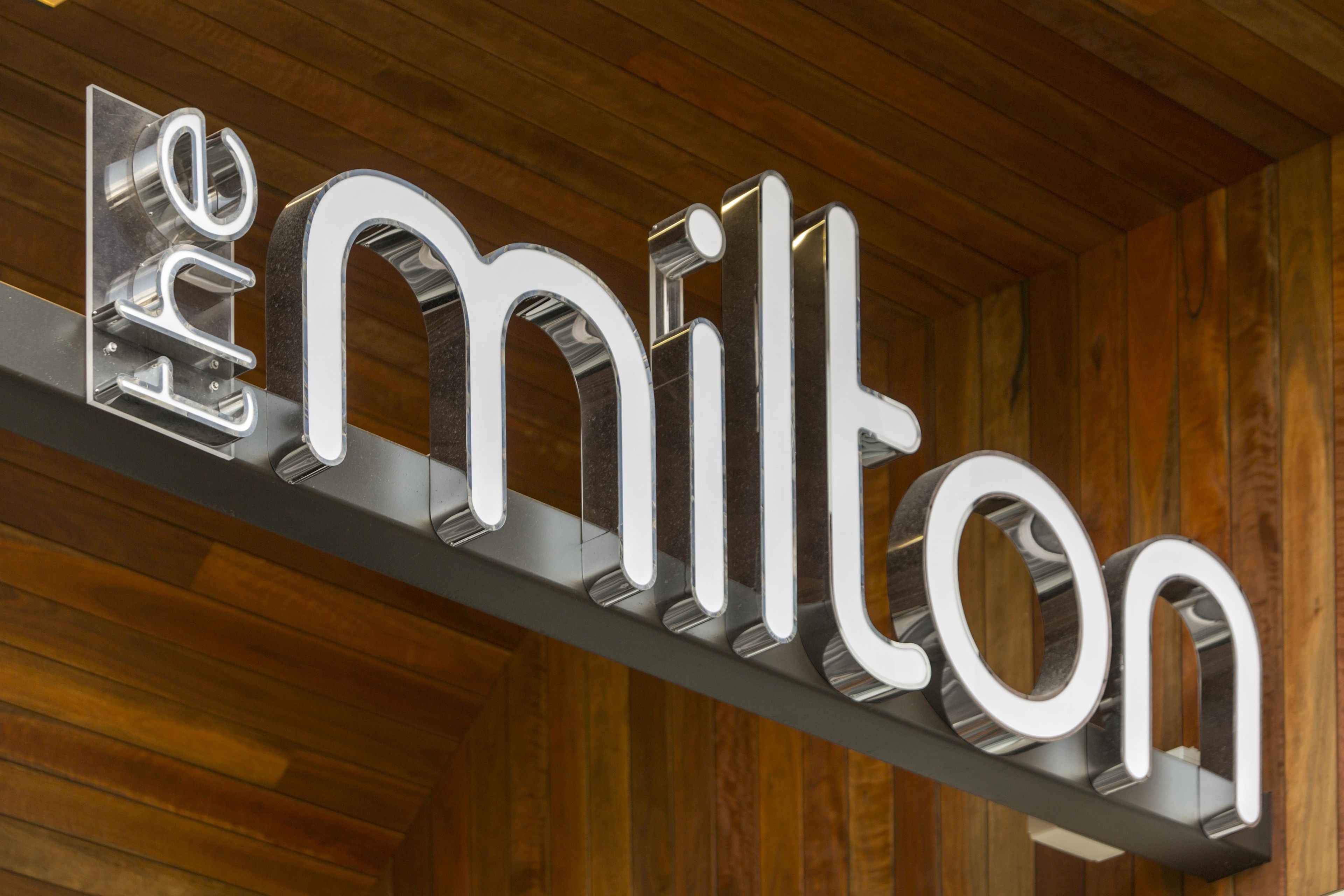 Ein metallisches Schild mit dem Schriftzug 'emilton' an einer Holzwand befestigt.
