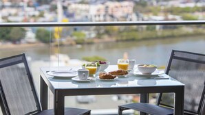 A breakfast table with croissants, fruit, and juice, overlooking a river with buildings in the background.