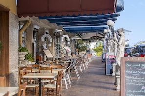 An outdoor café with tables and chairs, a covered seating area, and a sign for 'Little Paris Restaurant'. - The Milton Brisbane (Milton)