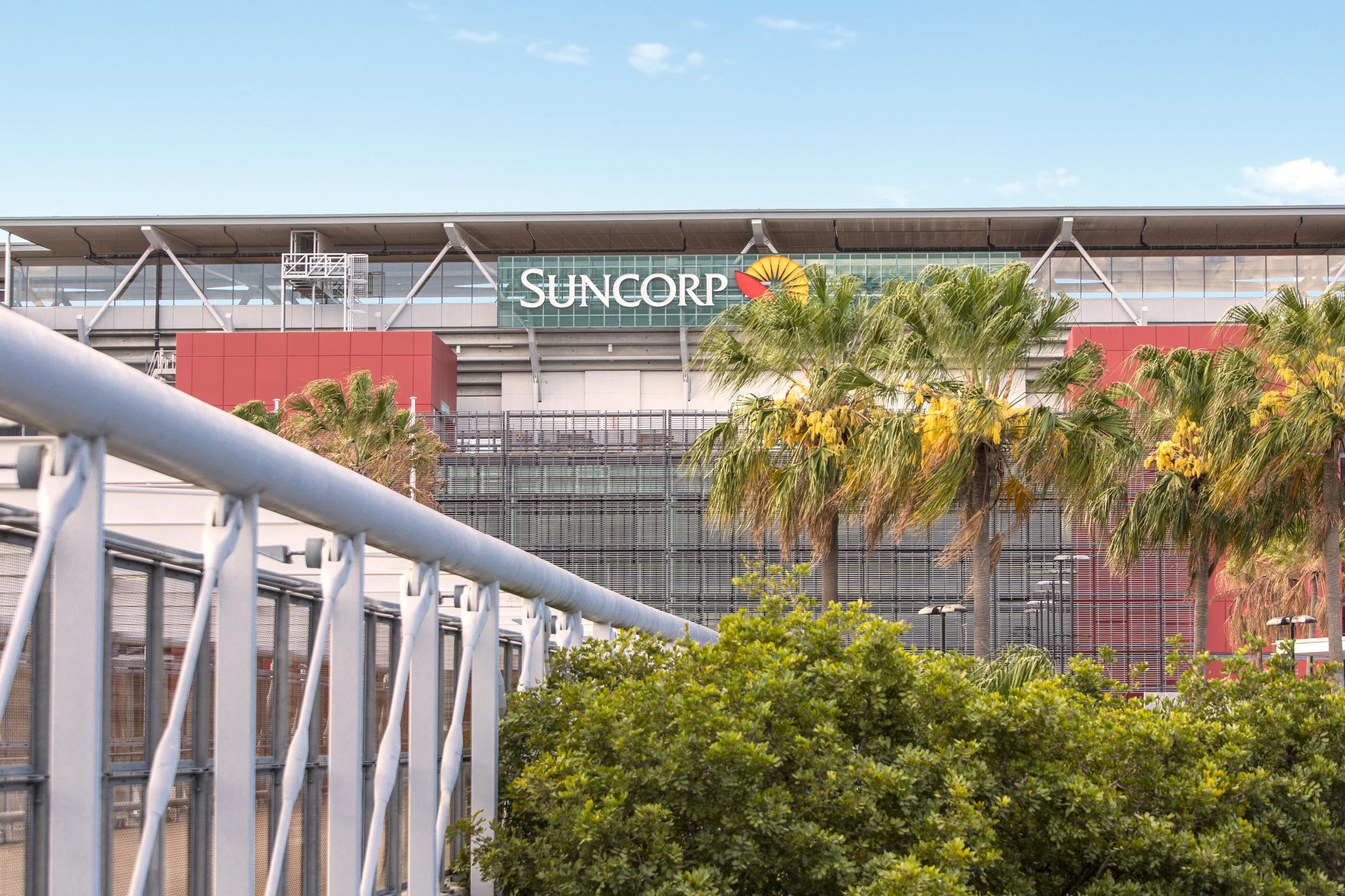A modern building with a prominent 'SUNCORP' sign, surrounded by palm trees and metal railings.
