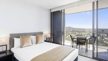 A modern hotel room with a large bed, a desk, and a balcony with a city view.
