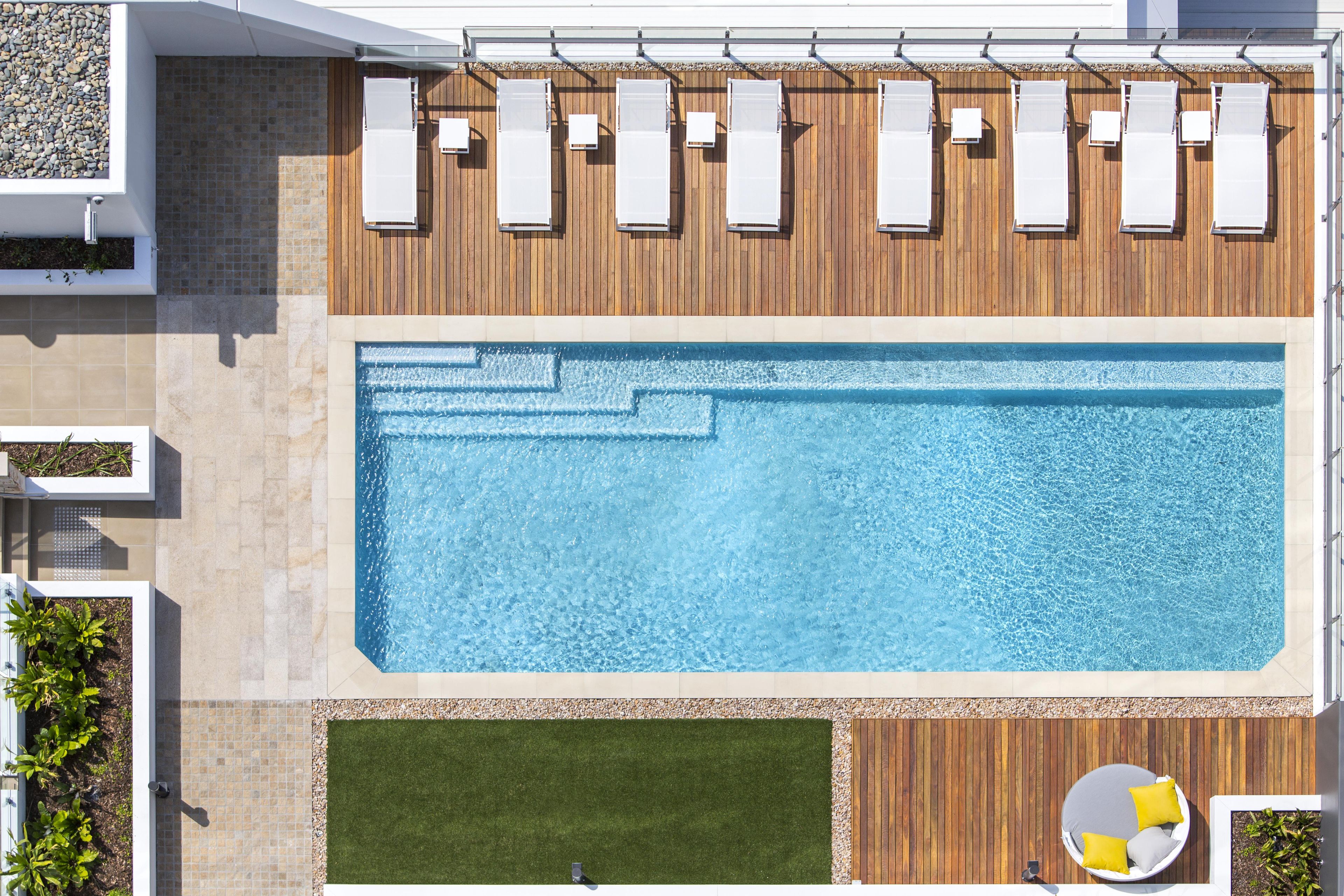 Una piscina en la azotea con terraza de madera, sillas de descanso y una zona de estar circular.