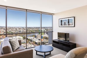 A modern living room with a large window, a sofa, a coffee table, and a flat-screen TV. - The Milton Brisbane (Milton)