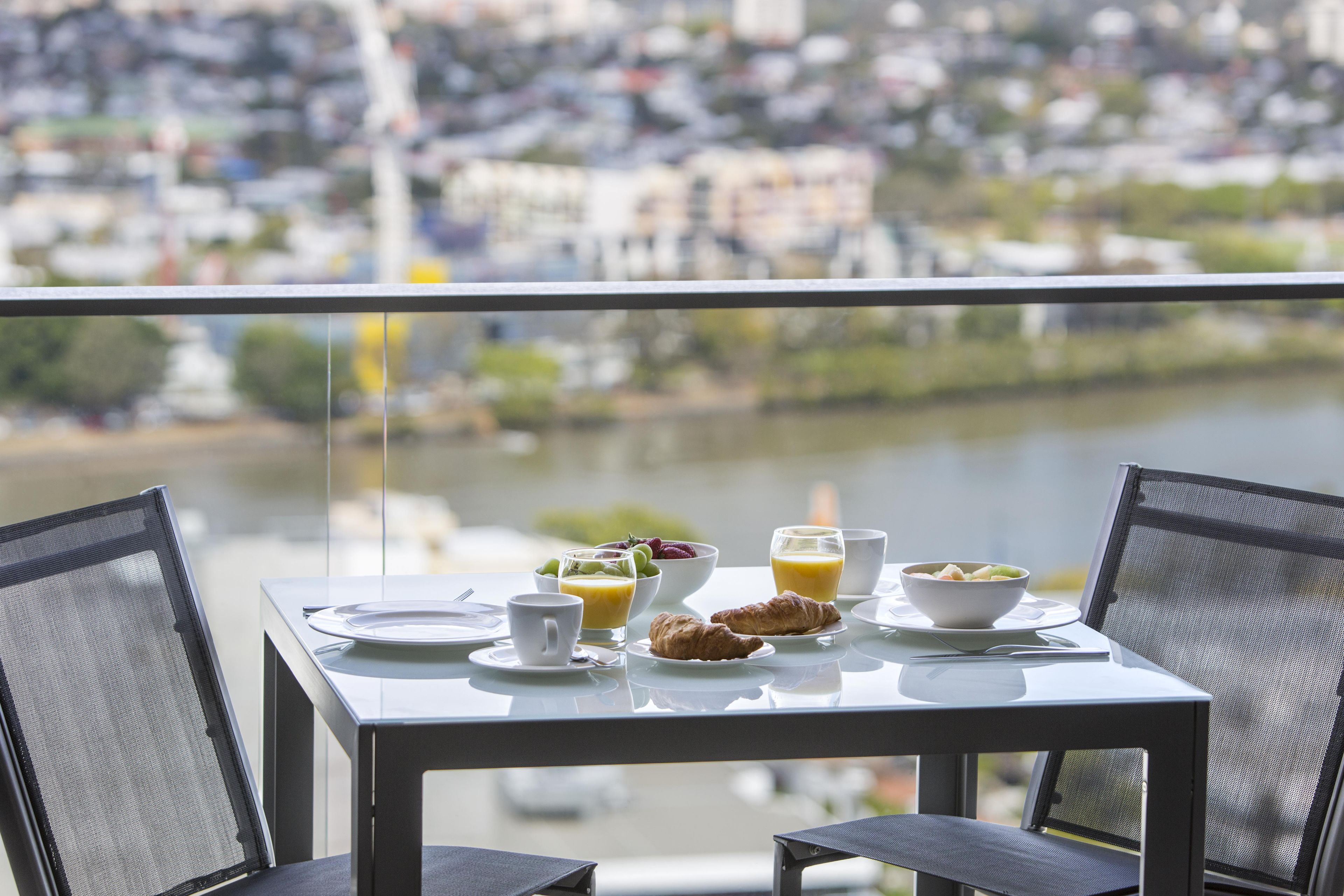 A dining table with breakfast items, two chairs, and a view of a river and cityscape.
