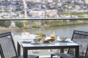 A dining table with breakfast items, two chairs, and a view of a river and cityscape. - The Milton Brisbane (Milton)