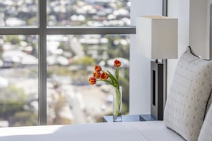 A hotel room with a large window, a bedside table with a vase of tulips, and a lamp. - The Milton Brisbane (Milton)