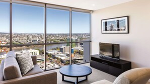 A modern living room with a large window offering a city view, a flat-screen TV, and a comfortable seating area.