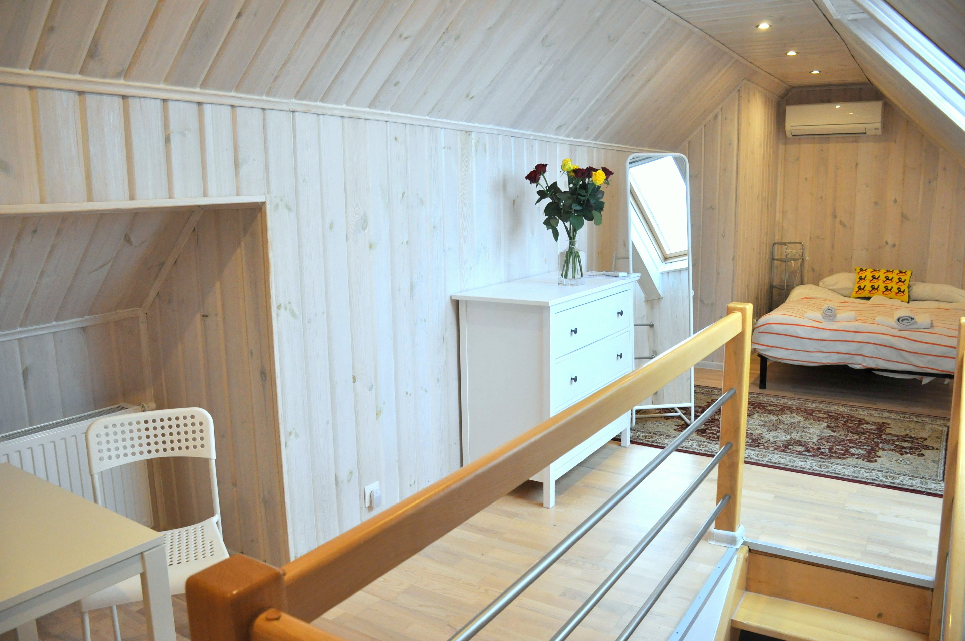 A bedroom with a wooden ceiling, a white dresser, a bed with a striped blanket, and a small table with a chair.