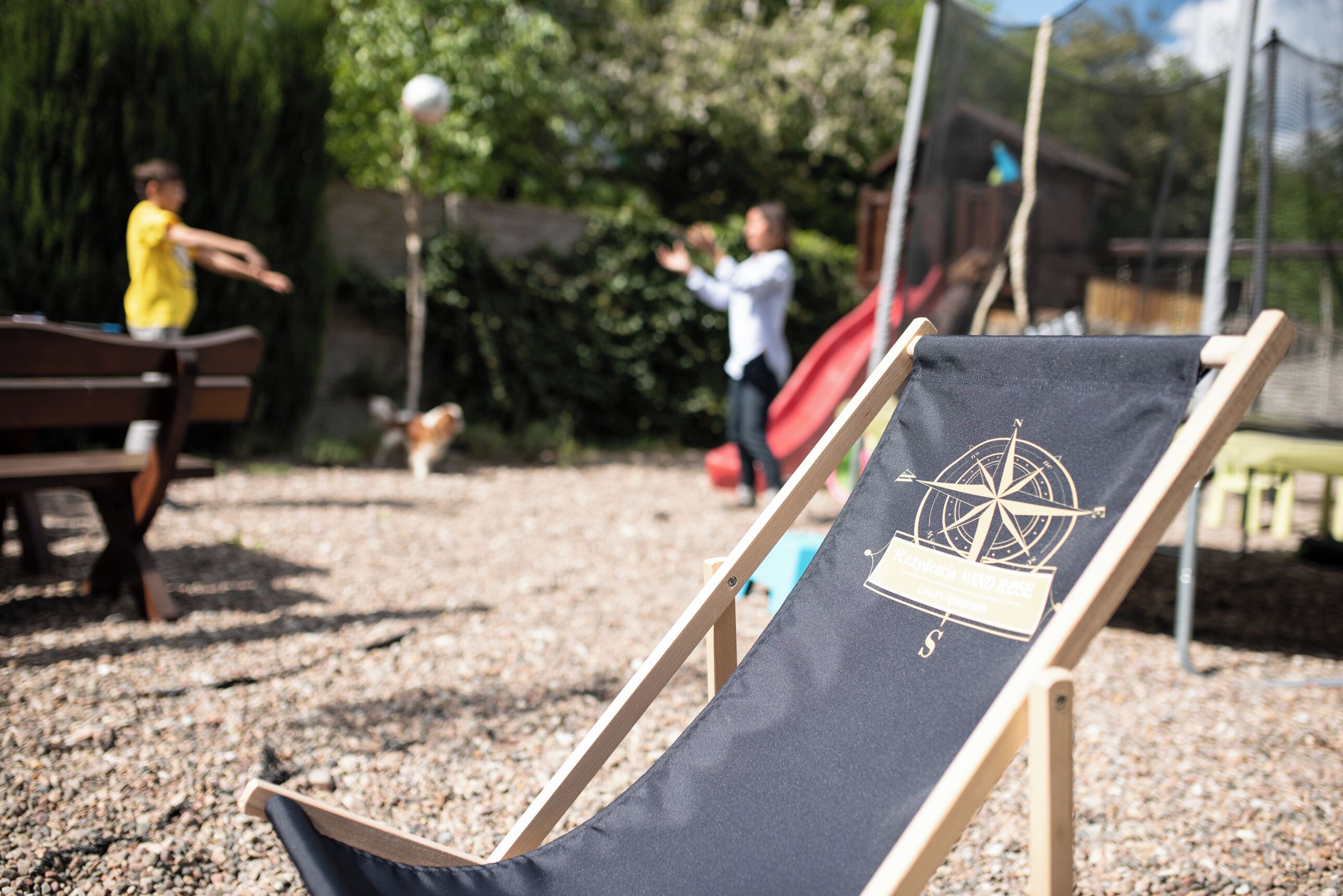 Una sedia da spiaggia con un motivo a bussola, una panchina in legno e uno scivolo rosso in un giardino.