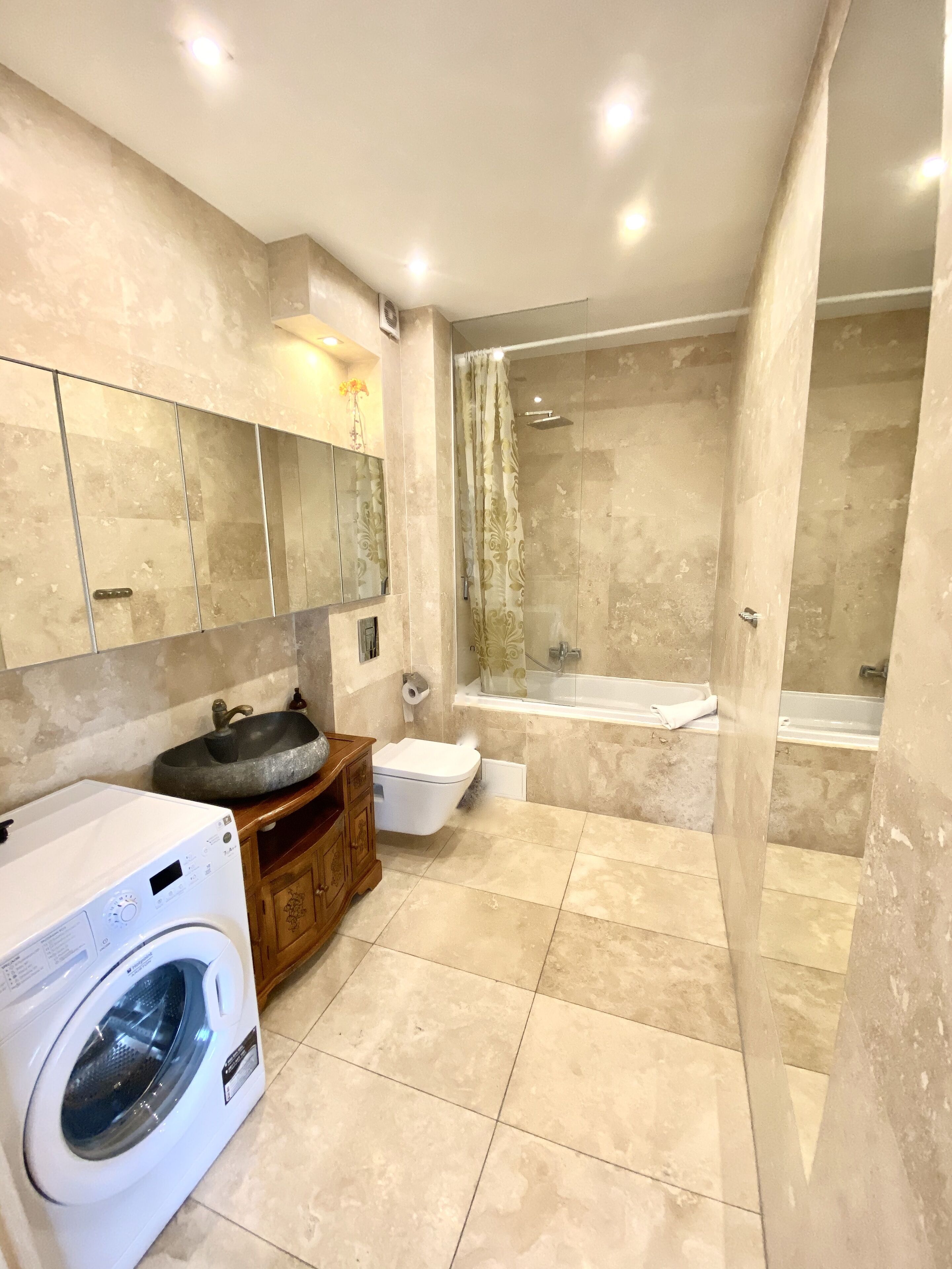 A modern bathroom with a built-in washing machine, a sink, a toilet, and a shower area.