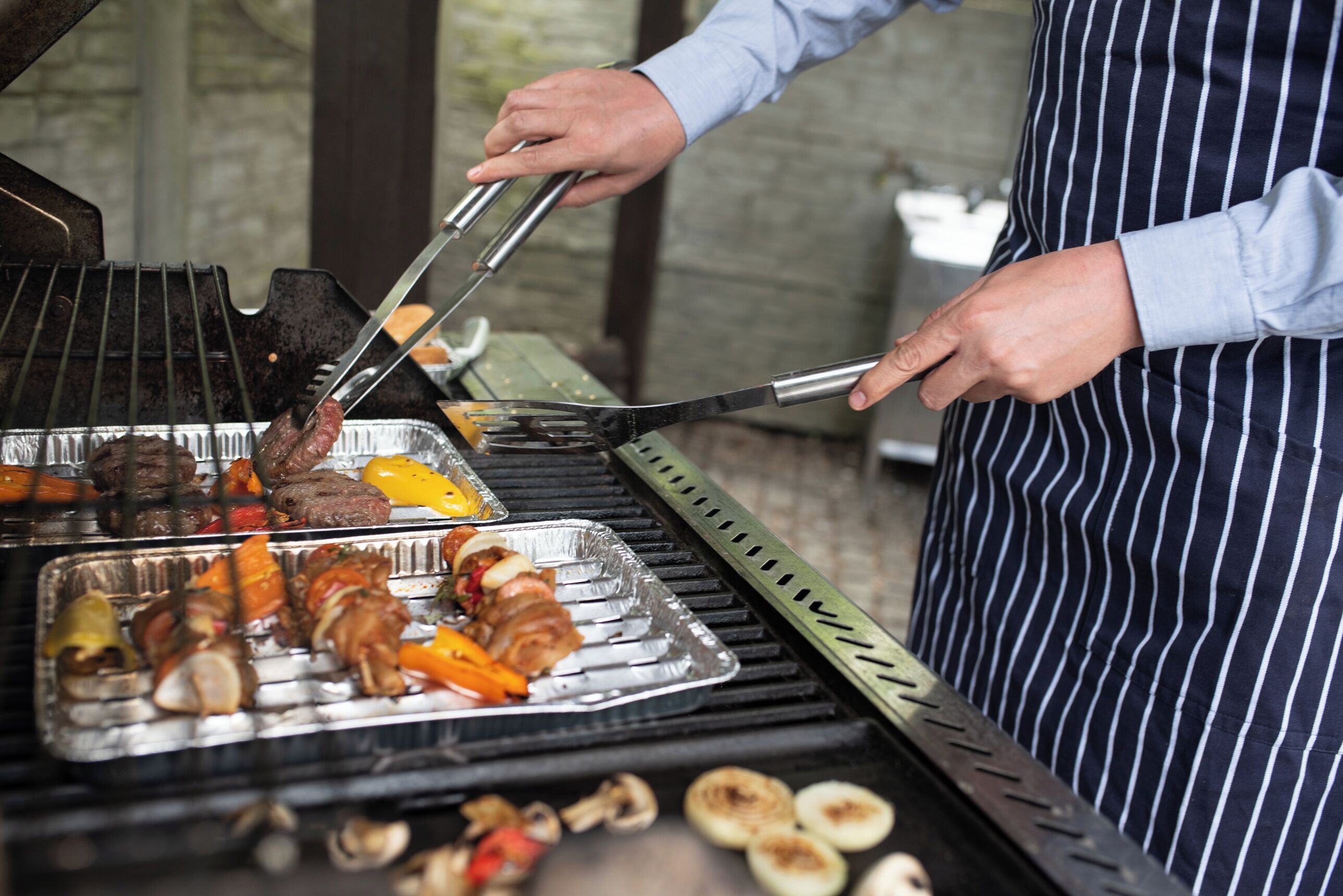 A person grilling various meats and vegetables on an outdoor grill.