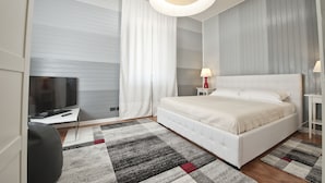 A modern hotel room with a large bed, a flat-screen TV, a desk, and a large window with curtains. - Verona Maison (Verona)