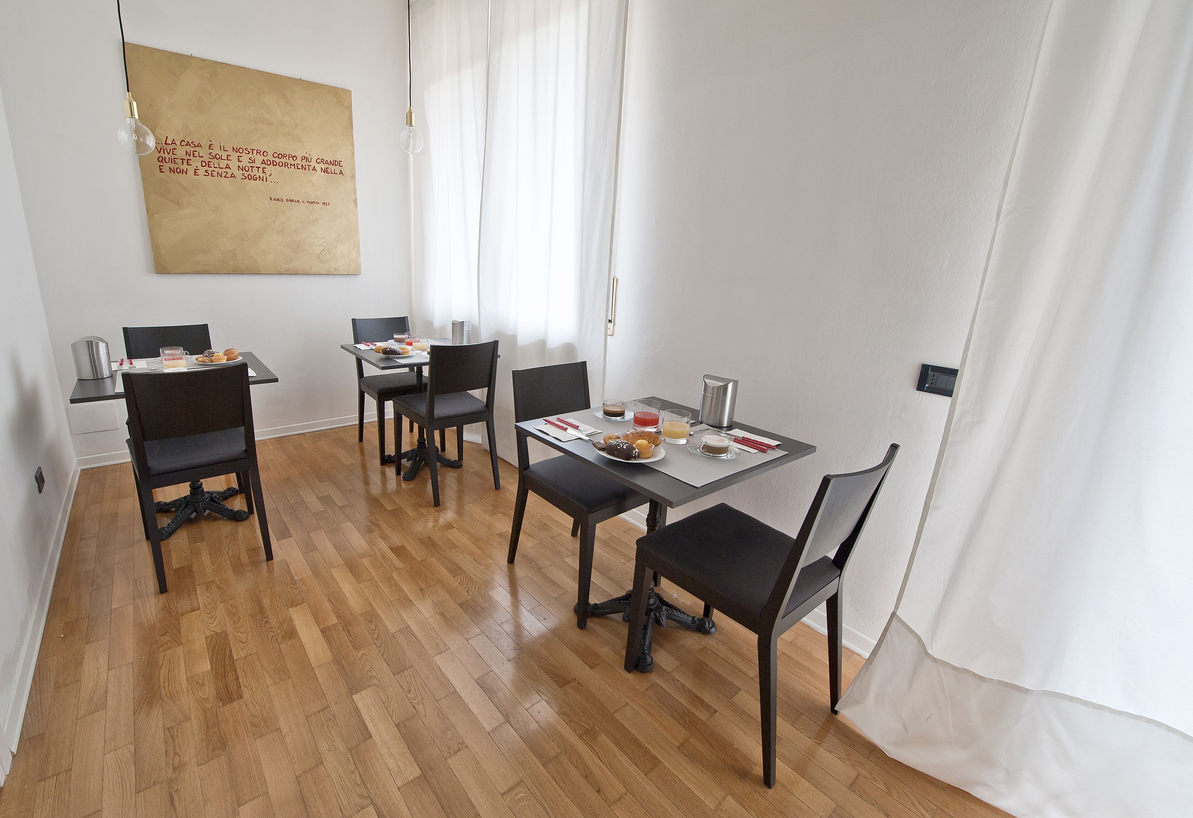 A dining area with a wooden floor, a table with chairs, a painting on the wall, and a window with curtains.