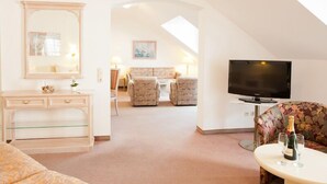 A spacious room with a large mirror, a flat-screen TV, a sofa, and a small table with a bottle and glasses. - Hoteltraube Rudesheim (Ruedesheim am Rhein)