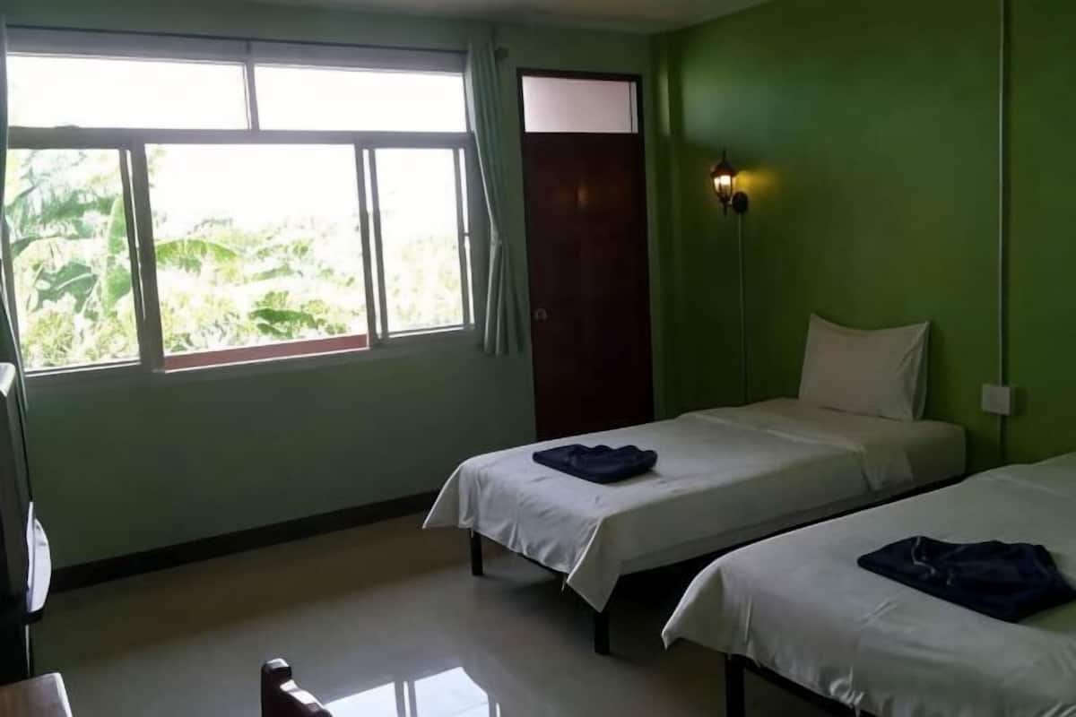 A room with two beds, a window with curtains, a bedside lamp, and a door.