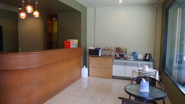 A hotel reception area with a wooden reception desk, a microwave, and a small dining area with a table and chairs. - U Sabuy Mansion Trang (Trang)