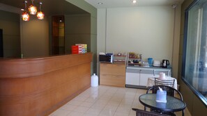 A hotel reception area with a wooden reception desk, a microwave, and a small dining area with a table and chairs. - U Sabuy Mansion Trang (Trang)