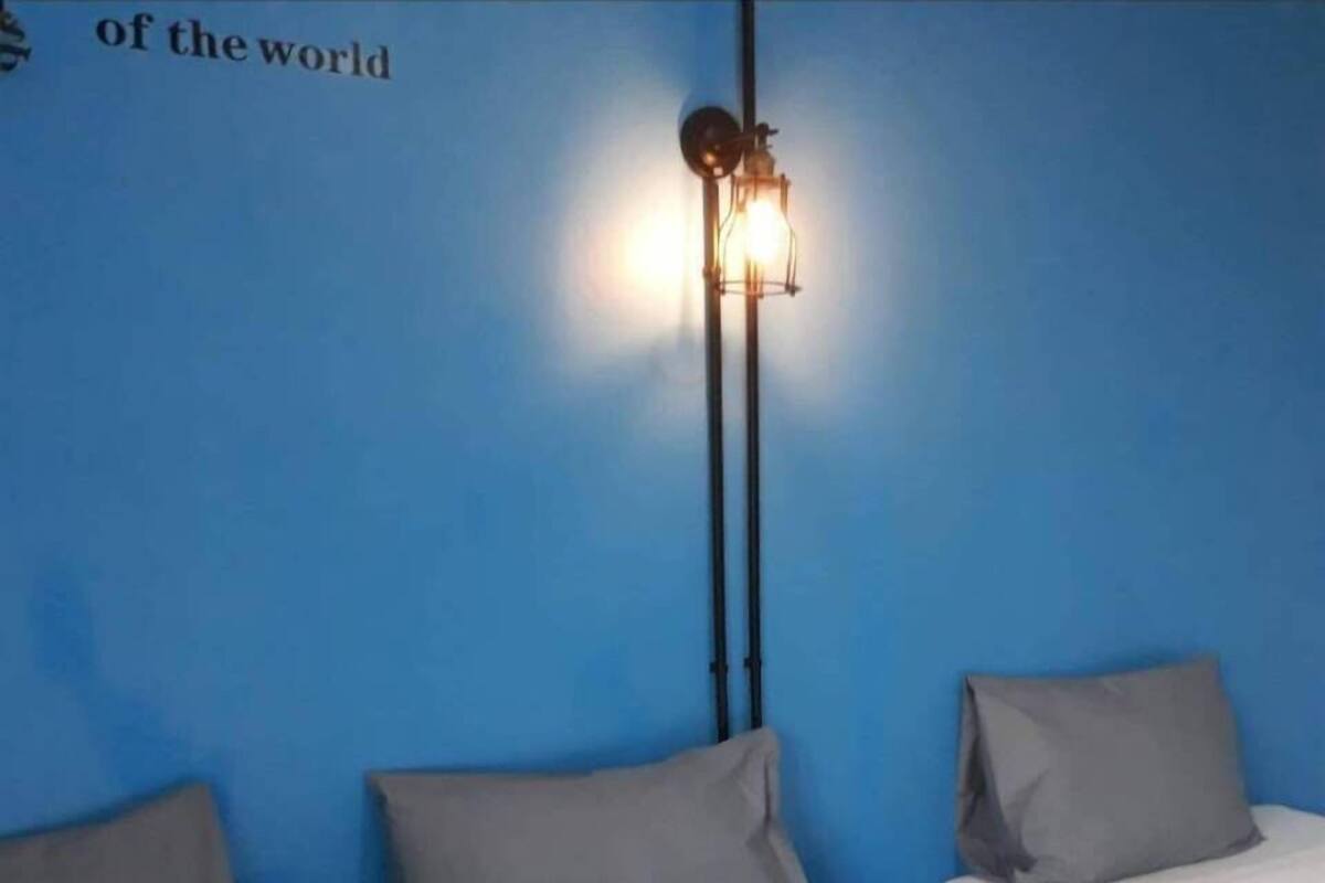 A room with two beds, a blue wall, and a wall-mounted light fixture.
