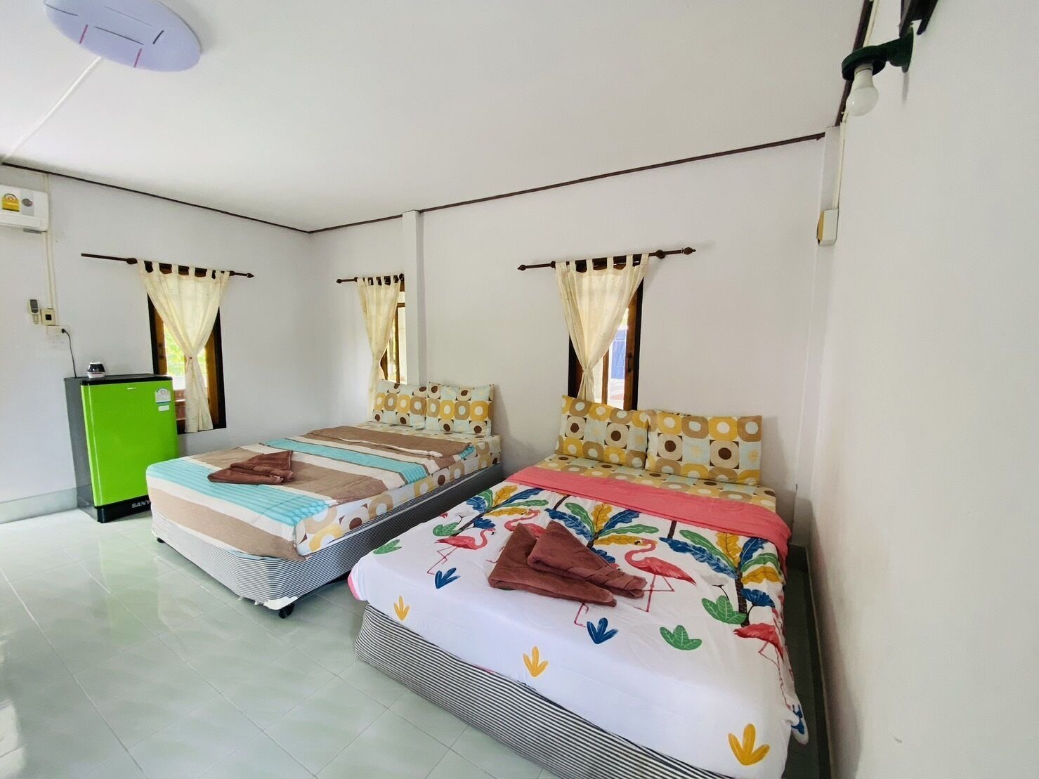 A room with two beds, a refrigerator, and a ceiling fan.