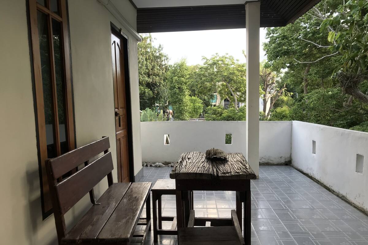 A wooden bench and table on a tiled patio with a white wall and trees in the background.