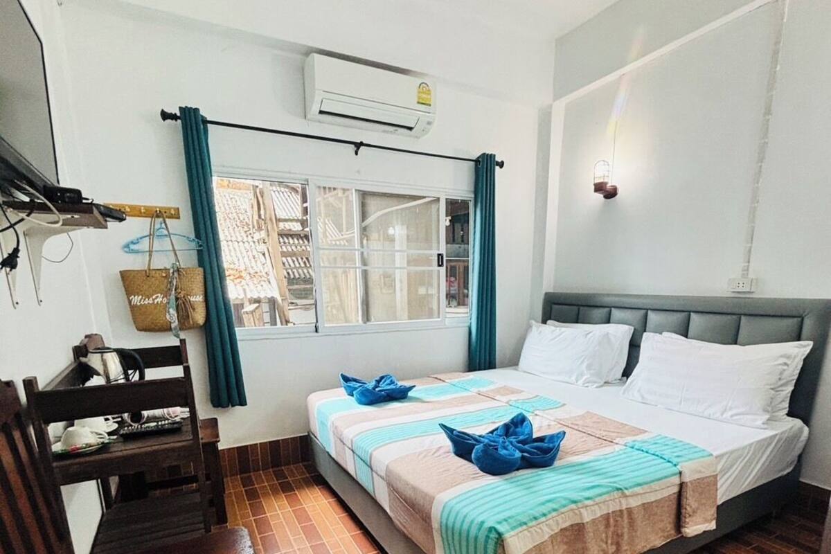 A bedroom with a bed, a desk, a chair, a window with curtains, and an air conditioning unit.