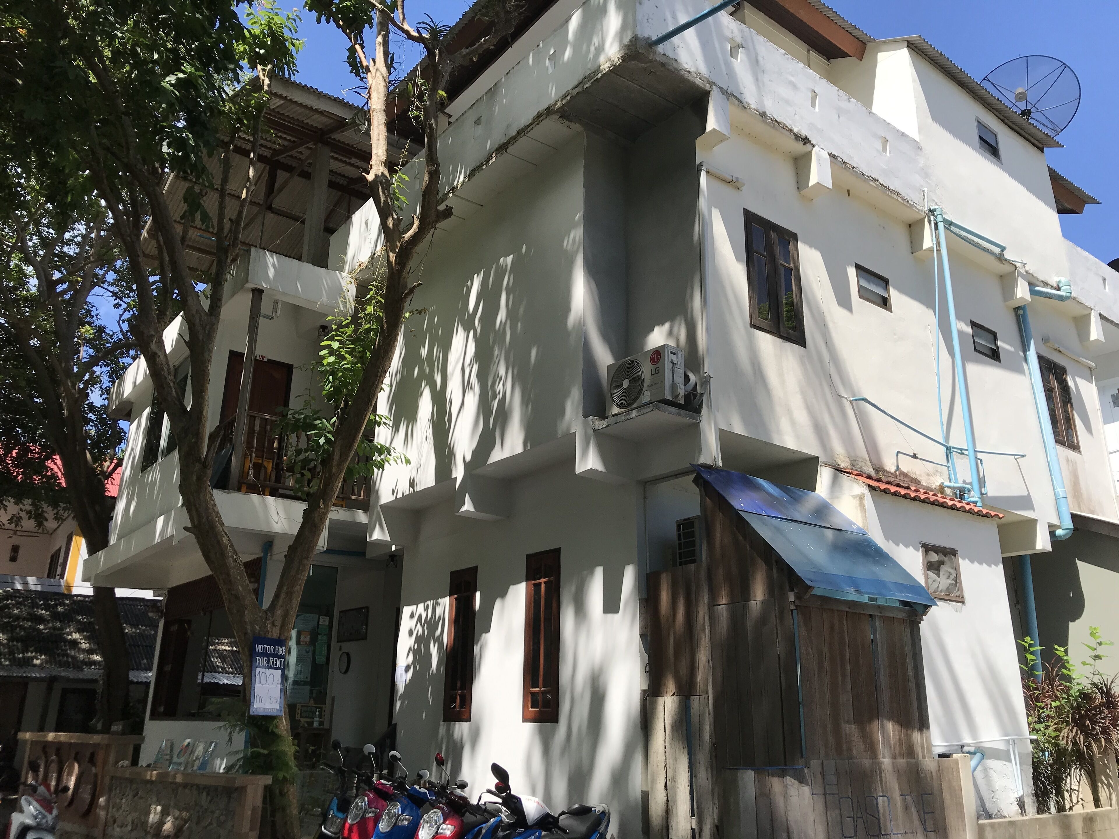 A multi-story building with a white facade, a satellite dish, and a blue awning.