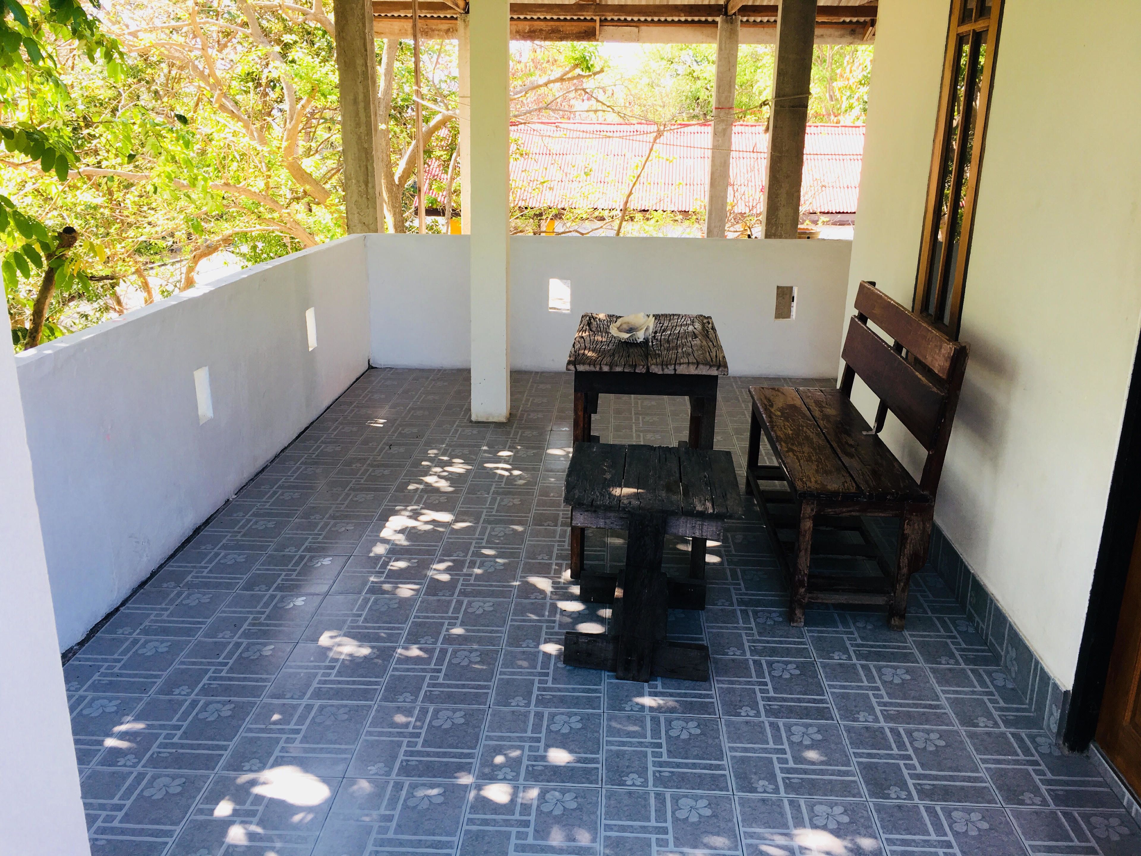 A covered outdoor area with a tiled floor, a wooden bench, and a table.