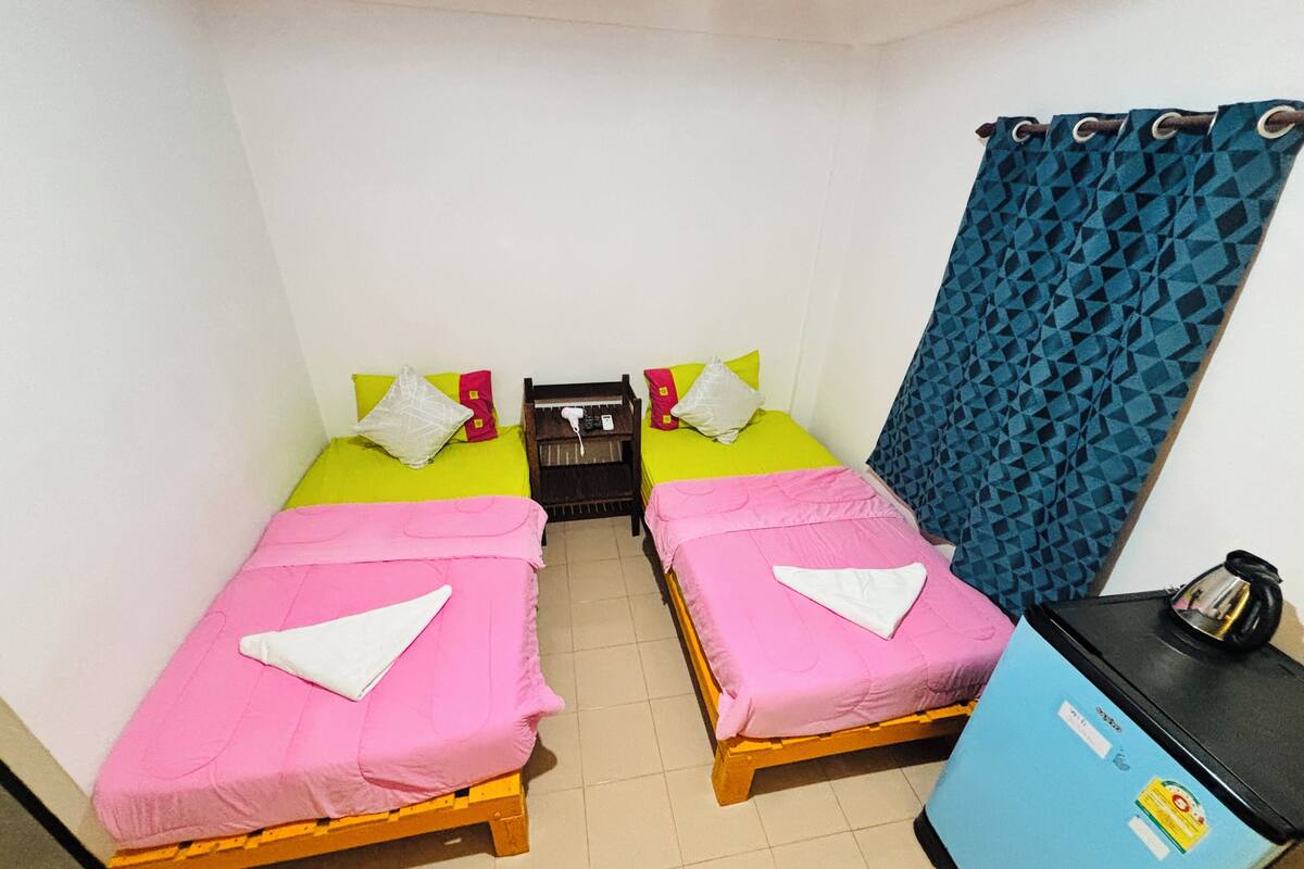 A small, clean room with two beds, a desk, and a blue curtain.