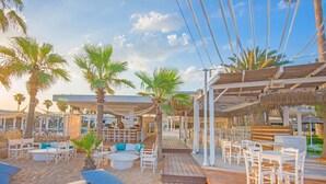 A beachside resort with wooden deck seating, palm trees, and a covered area with umbrellas. - Dome Beach Marina Hotel & Resort (Ayia Napa)
