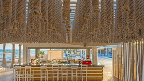 A beachside bar with wooden flooring, white bar stools, and a view of the ocean. - Dome Beach Marina Hotel & Resort (Ayia Napa)