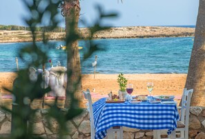 A table set for two with a blue and white checkered tablecloth, overlooking a beach with a rocky shoreline and calm sea. - Dome Beach Marina Hotel & Resort (Ayia Napa)