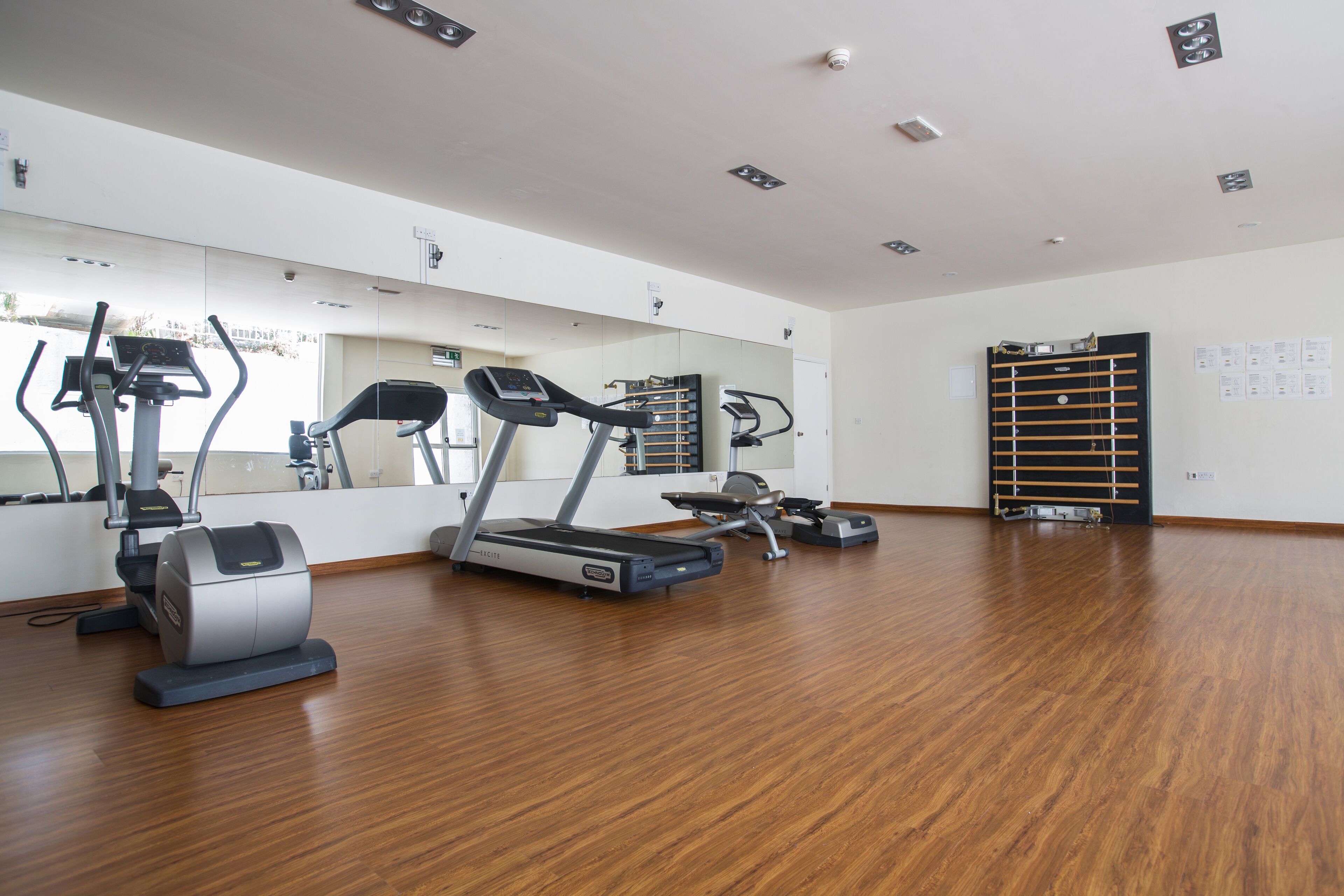 Un gimnasio con equipo de ejercicio, suelo de madera y un espejo grande.