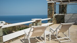 Una terraza con dos sillones blancos y un pilar de piedra, con vista al mar.