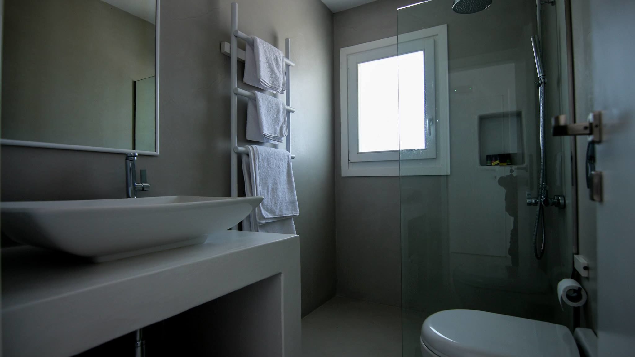 A modern bathroom with a large mirror, a white sink, a toilet, and a glass-enclosed shower.