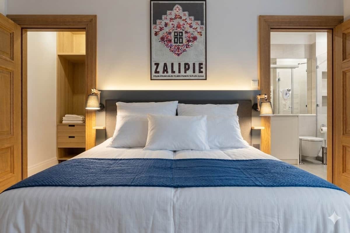 Una cama bien tendida con ropa de cama blanca y azul, una obra enmarcada encima y un armario de madera a la izquierda.