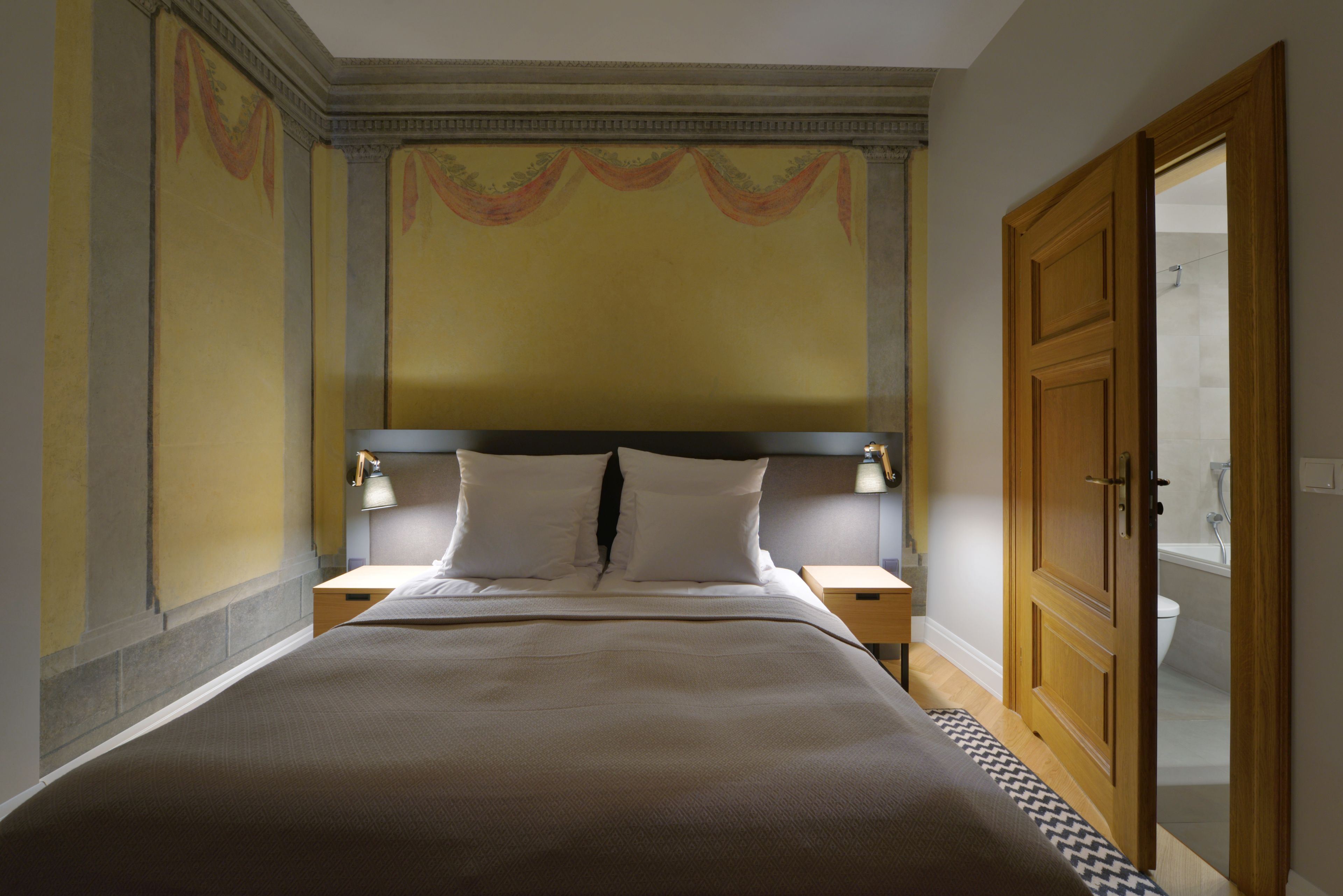 A hotel room with a large bed, two bedside tables with lamps, a wooden wardrobe, and a bathroom visible through an open door.