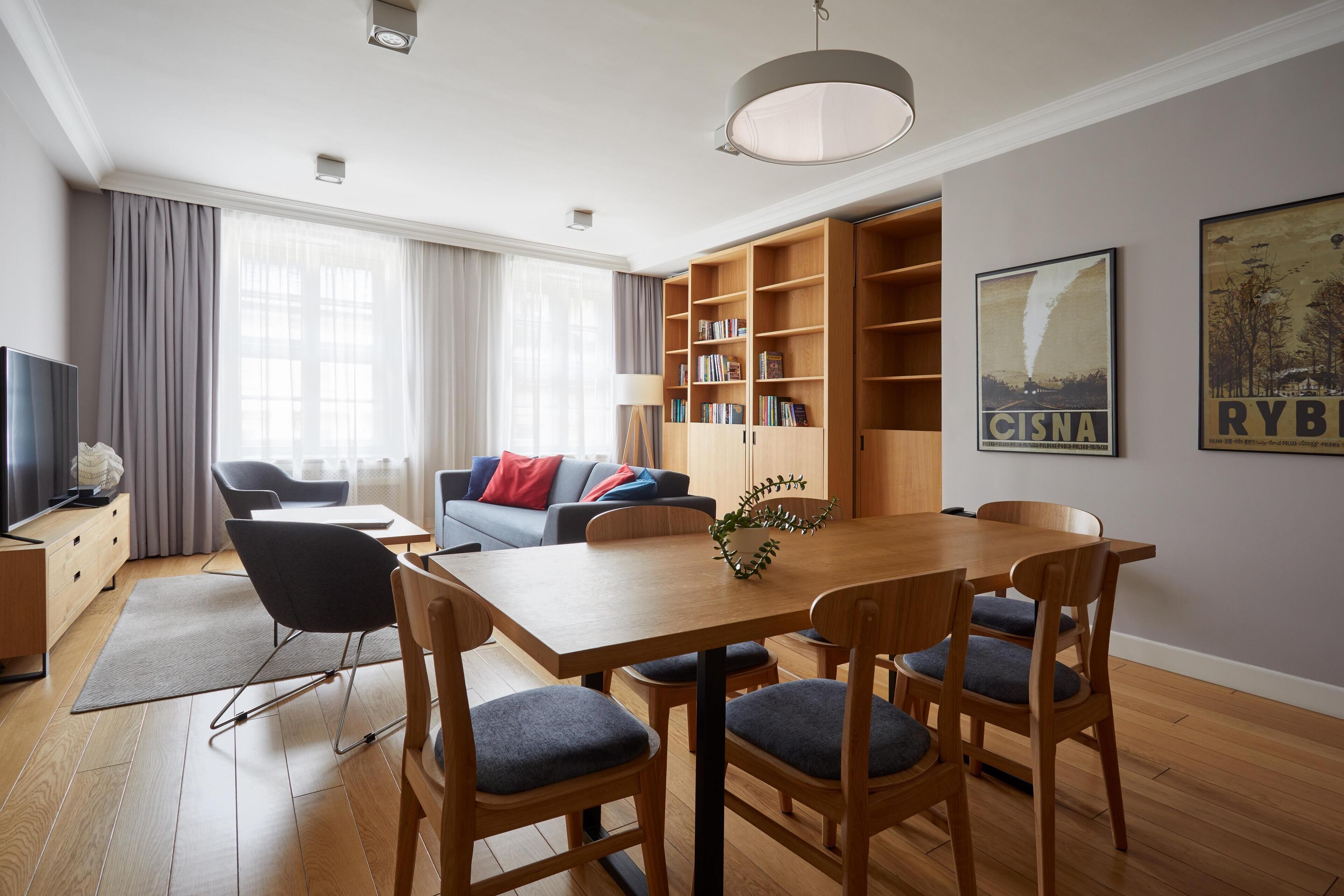 A modern living room with a dining area, wooden furniture, a bookshelf, and a television.