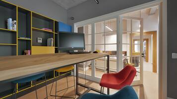 A modern room with a wooden desk, a flat-screen TV, and colorful chairs.