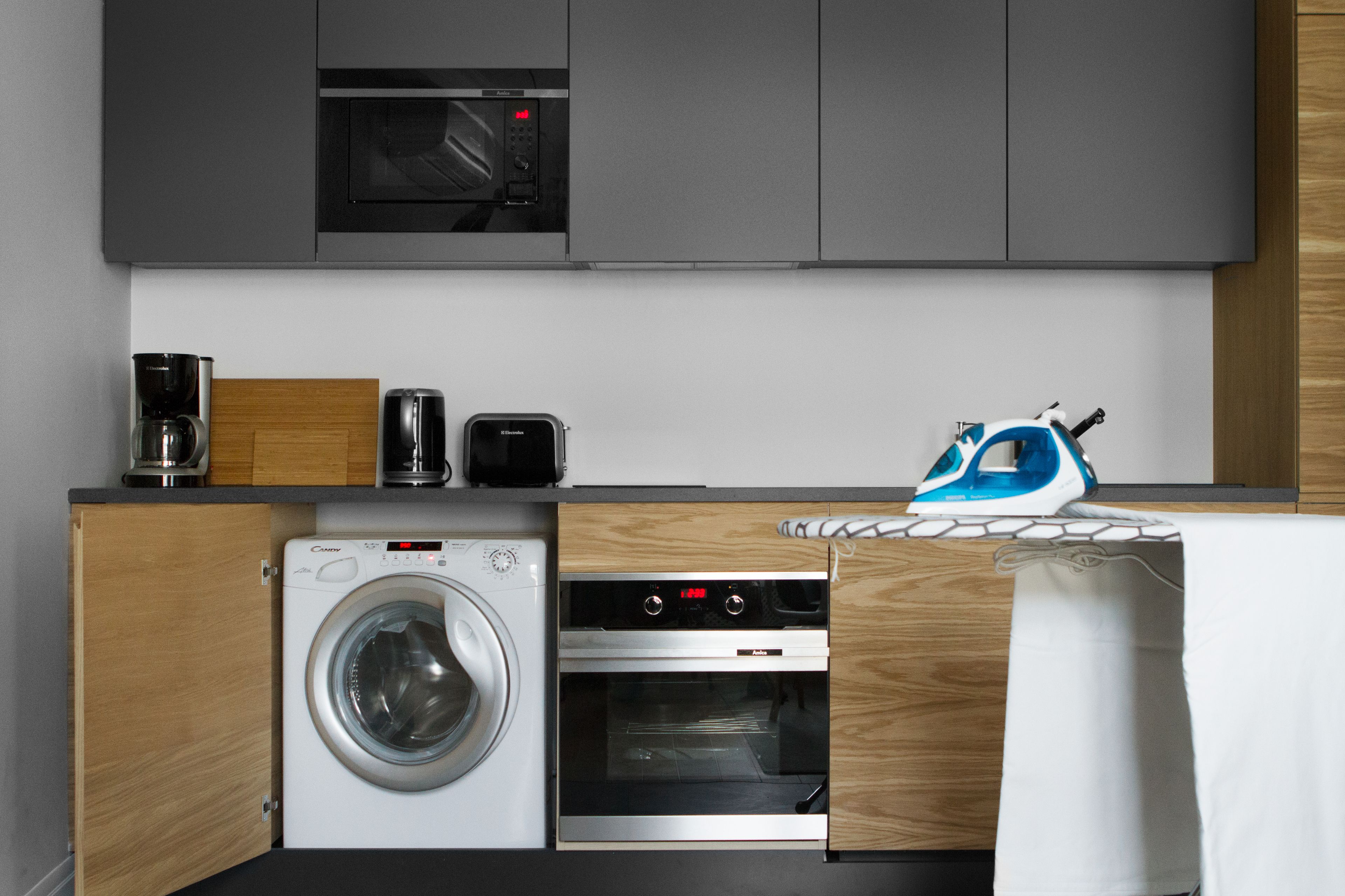 A compact kitchen with a washing machine, oven, microwave, and a coffee maker.