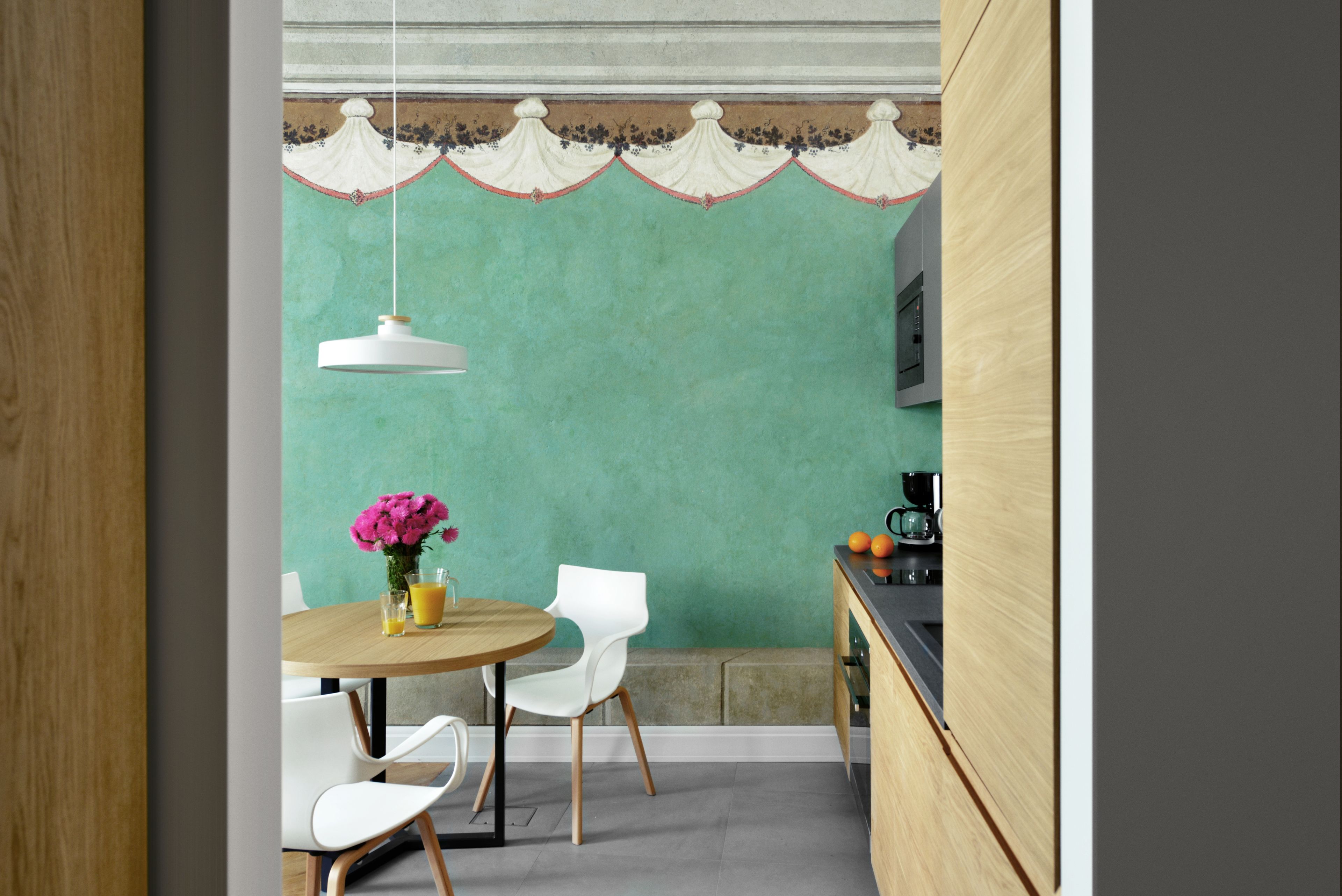 A dining area with a round table, white chairs, a vase with flowers, and a hanging light fixture.