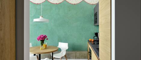 A dining area with a round table, white chairs, a vase with flowers, and a hanging light fixture.