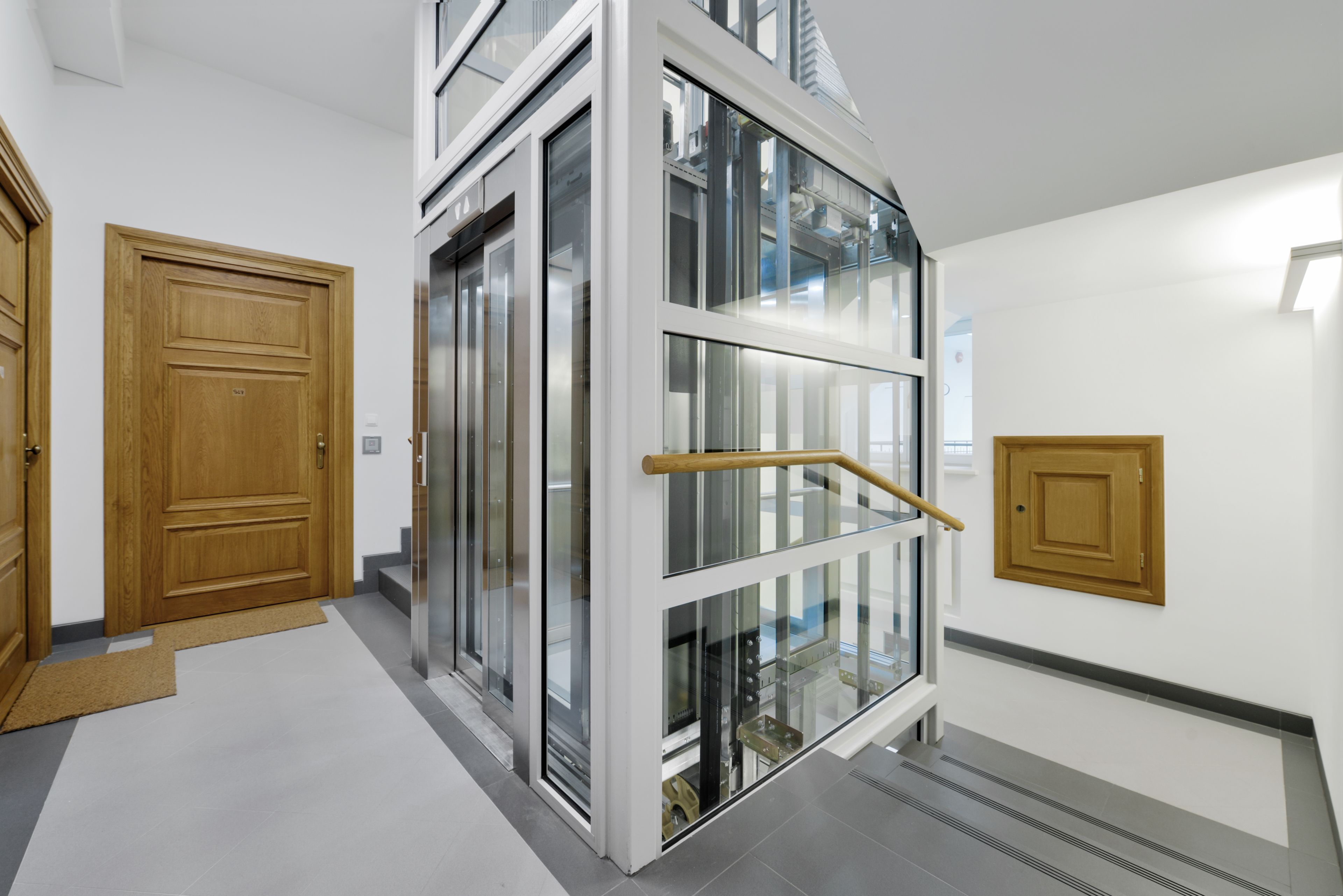A modern interior with a glass elevator, wooden doors, and a tiled floor.