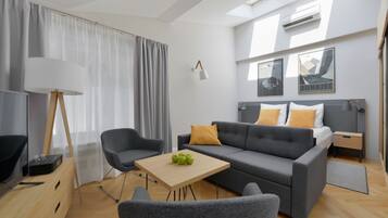 A modern living room with a grey sofa, a wooden coffee table with green apples, a grey armchair, a floor lamp, and a TV on a wooden cabinet.