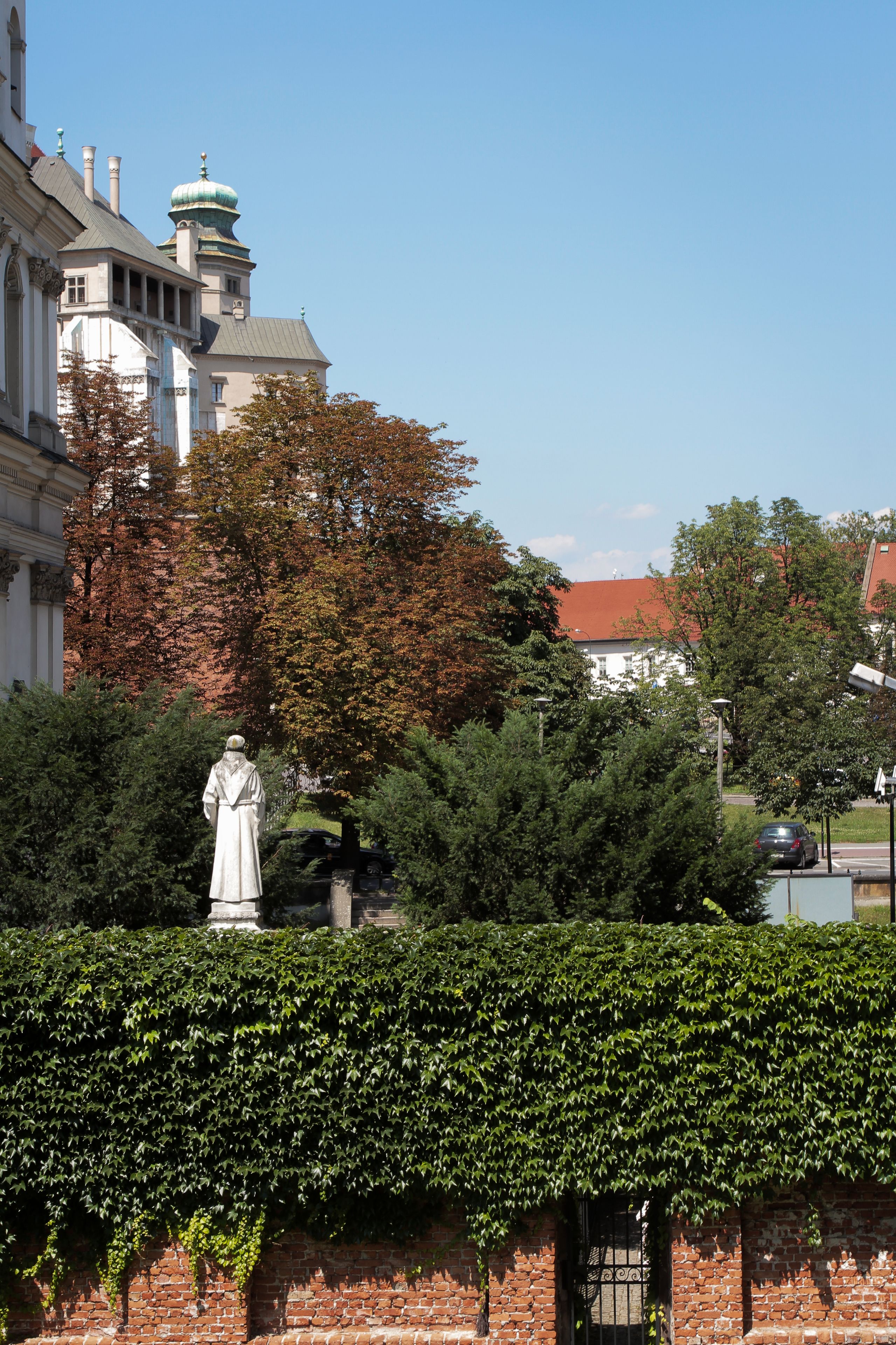 A statue in a garden with a brick wall and a building with a dome in the background.